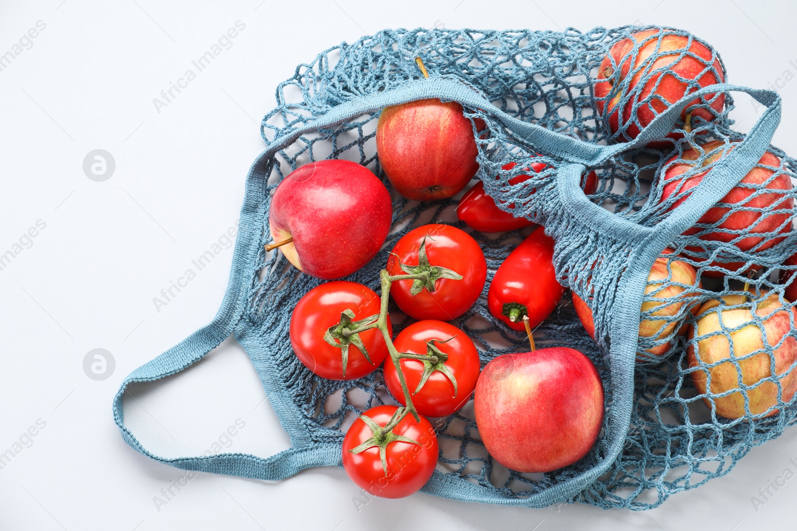 Photo of String bag with vegetables and apples on light grey background, top view