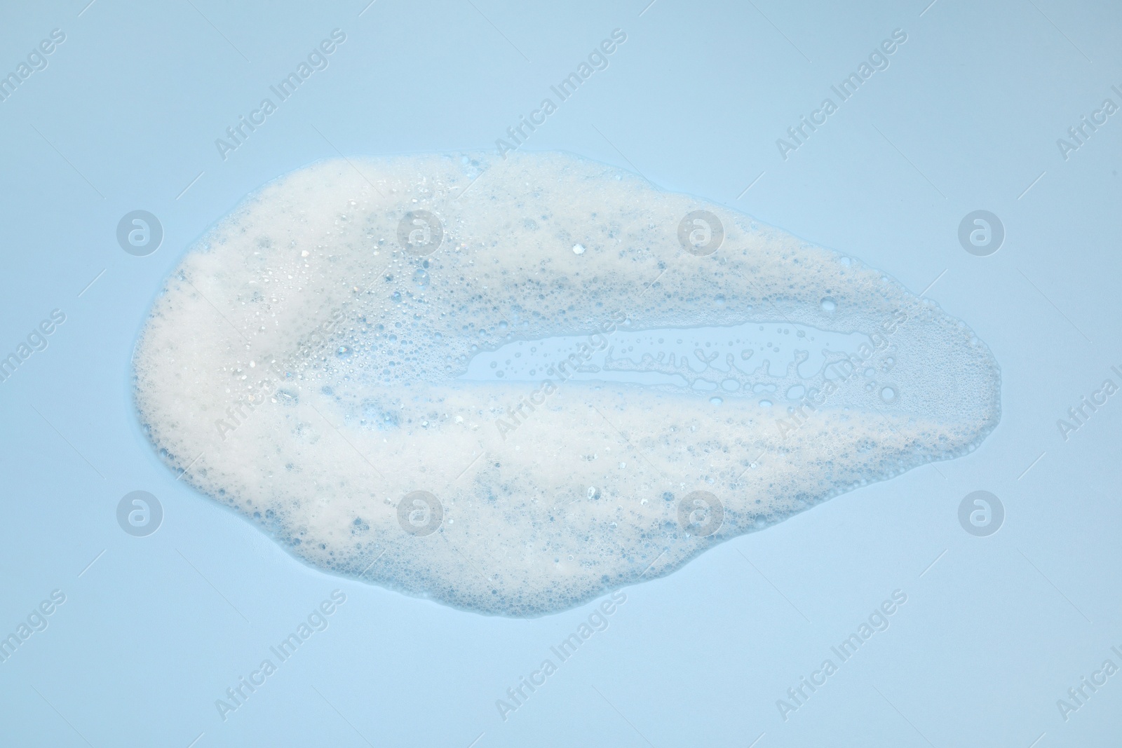 Photo of Smudge of white washing foam on light blue background, top view