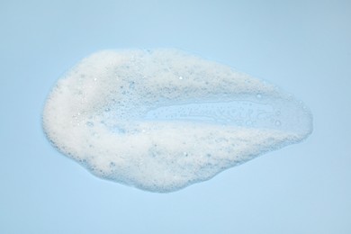 Photo of Smudge of white washing foam on light blue background, top view
