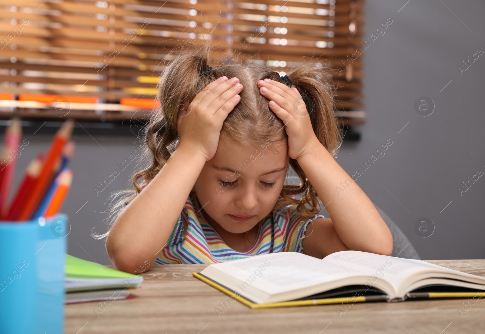 Photo of Tired little girl at table. Doing homework