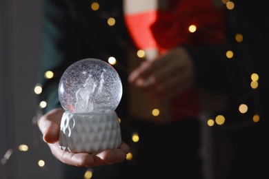 Photo of Woman holding Christmas snow globe on blurred background, closeup. Space for text