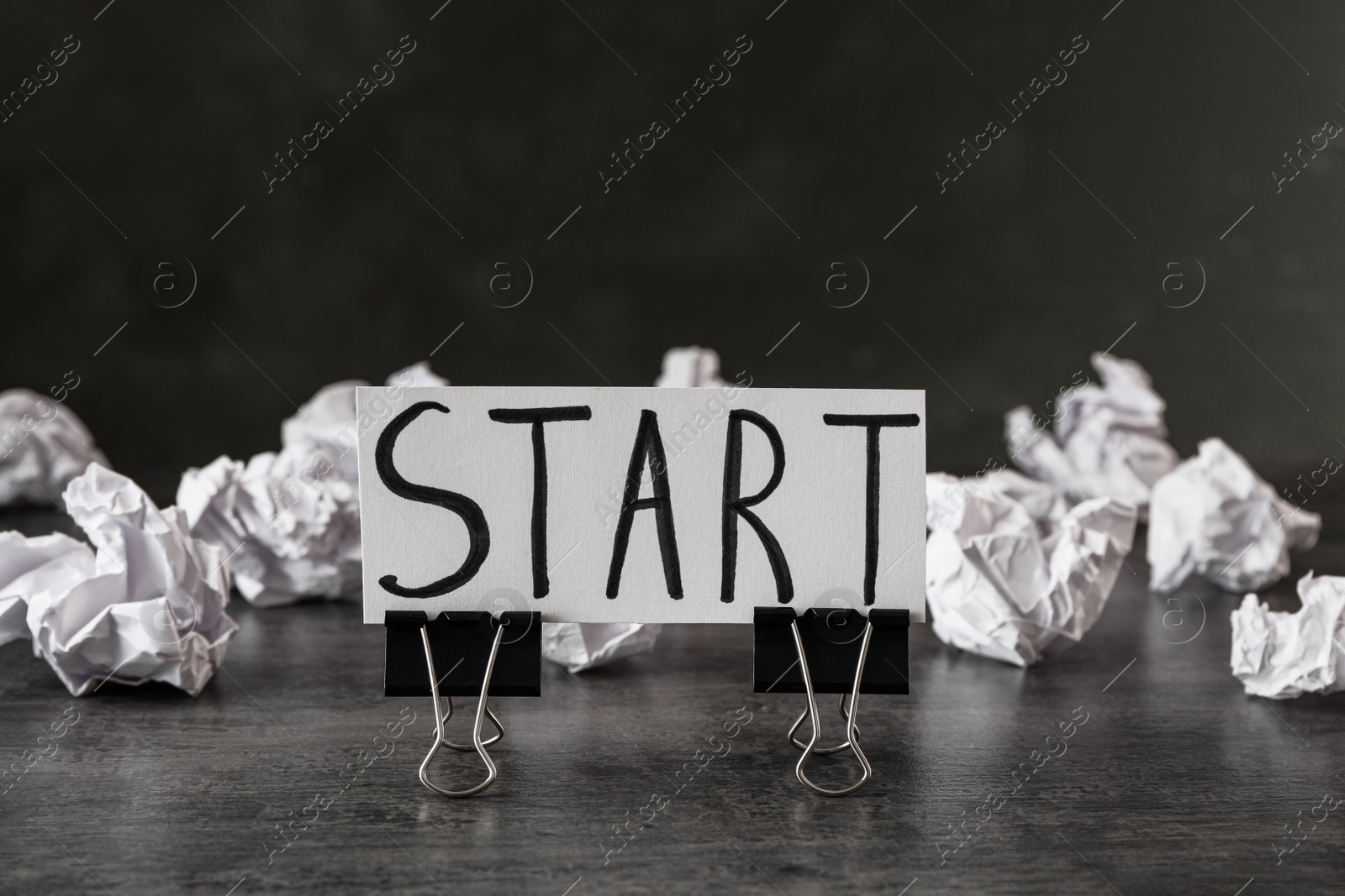 Photo of Sheet of paper with word Start and clips on grey stone table