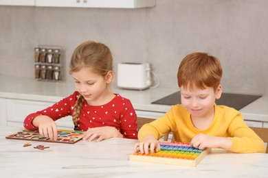Photo of Children playing with different math game kits at white marble table in kitchen. Study mathematics with pleasure