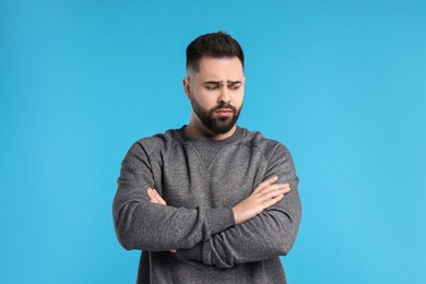 Photo of Portrait of sad man with crossed arms on light blue background