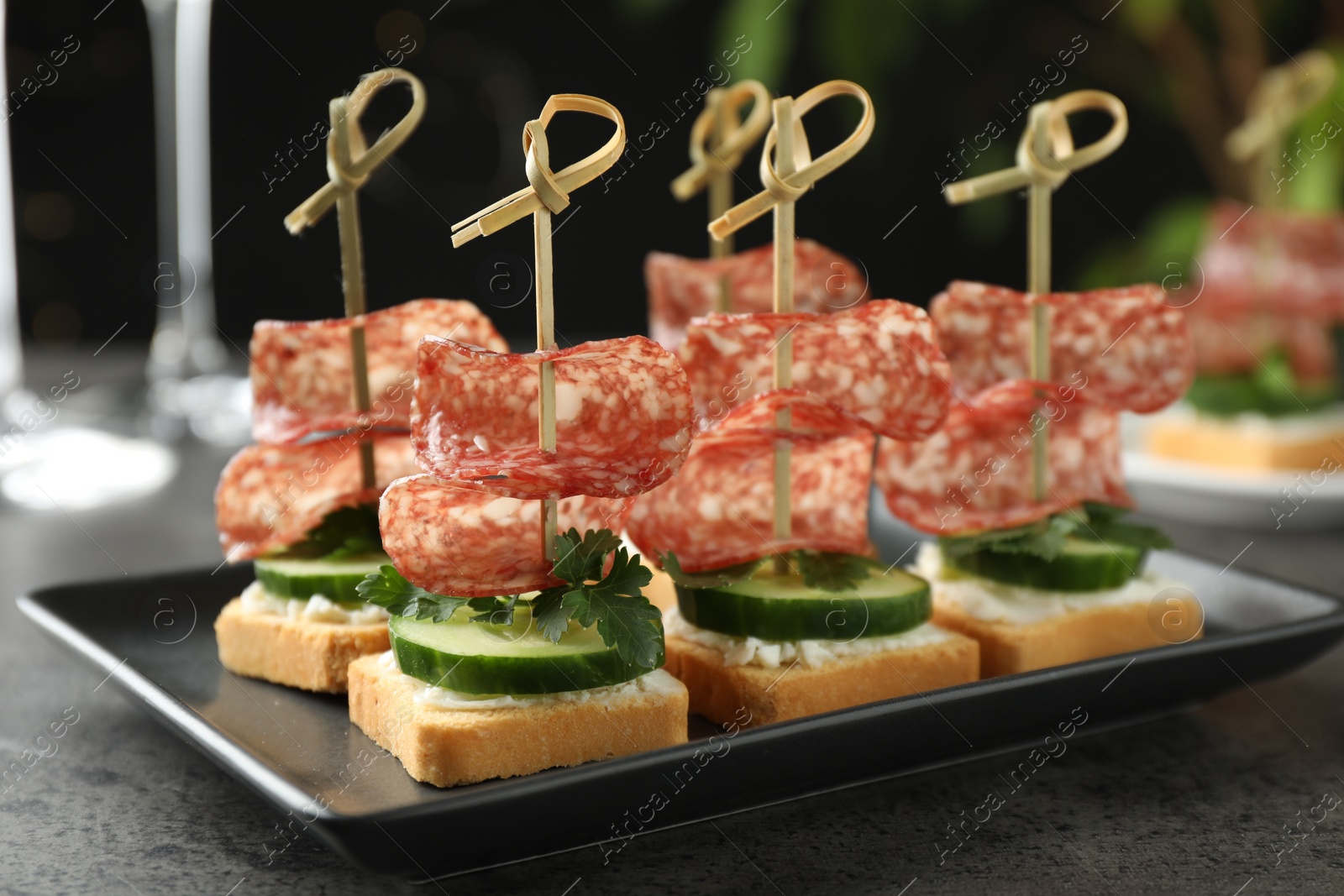 Photo of Tasty canapes with salami, cucumber and cream cheese on grey table, closeup