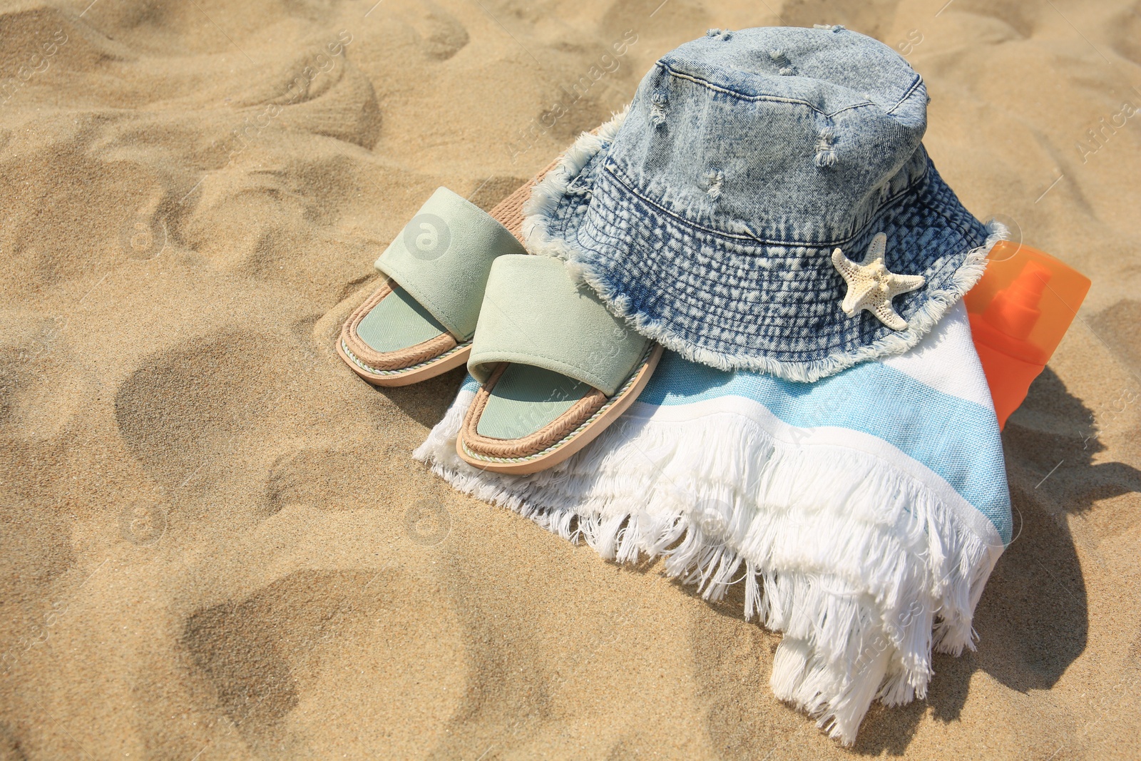 Photo of Denim hat, slippers, towel, starfish and sunscreen on sand. Space for text