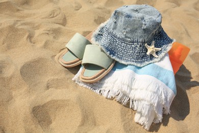 Denim hat, slippers, towel, starfish and sunscreen on sand. Space for text