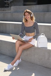 Photo of Young woman with stylish backpack and laptop on stairs outdoors