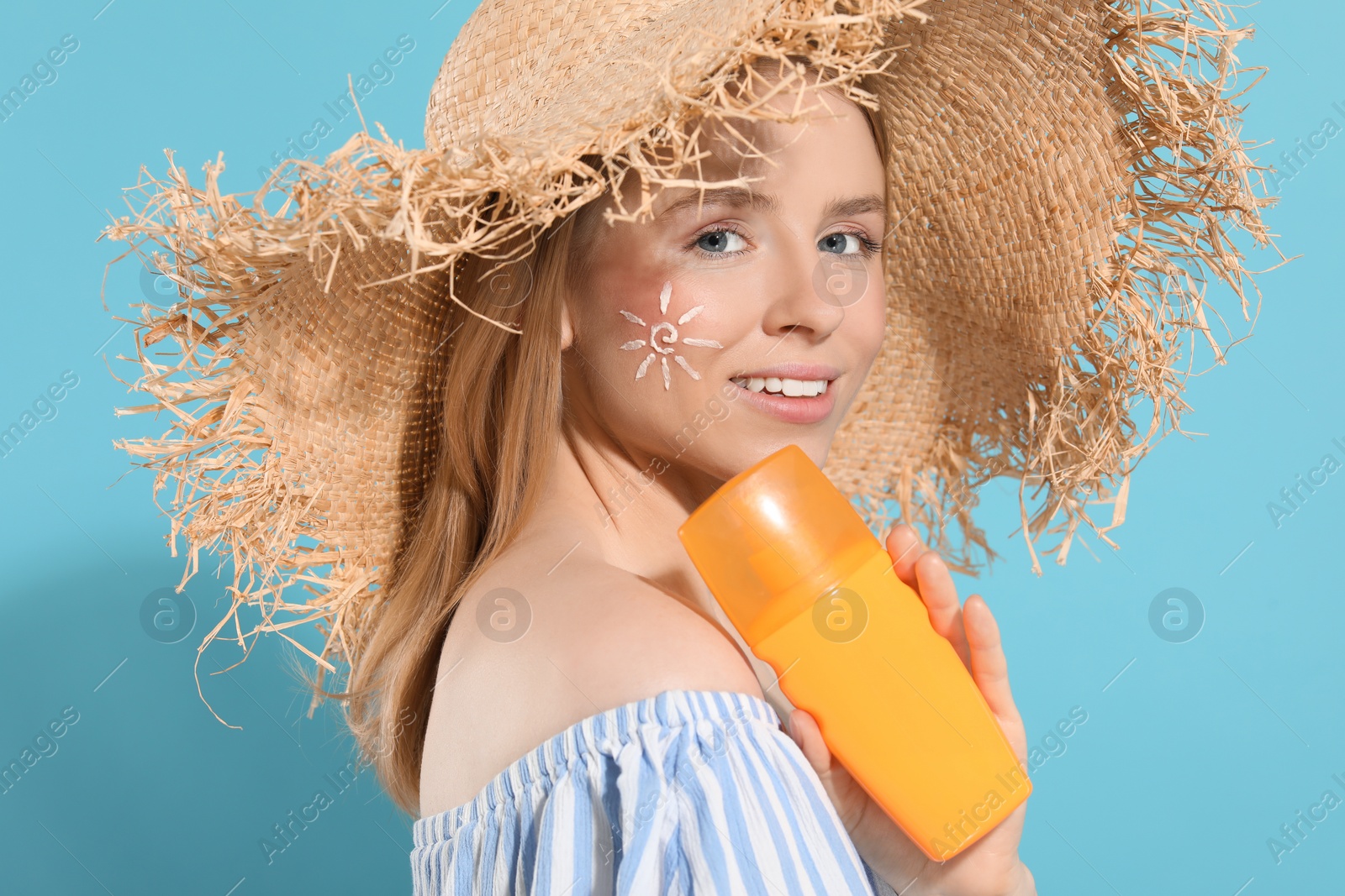 Photo of Beautiful young woman in straw hat with sun protection cream on light blue background