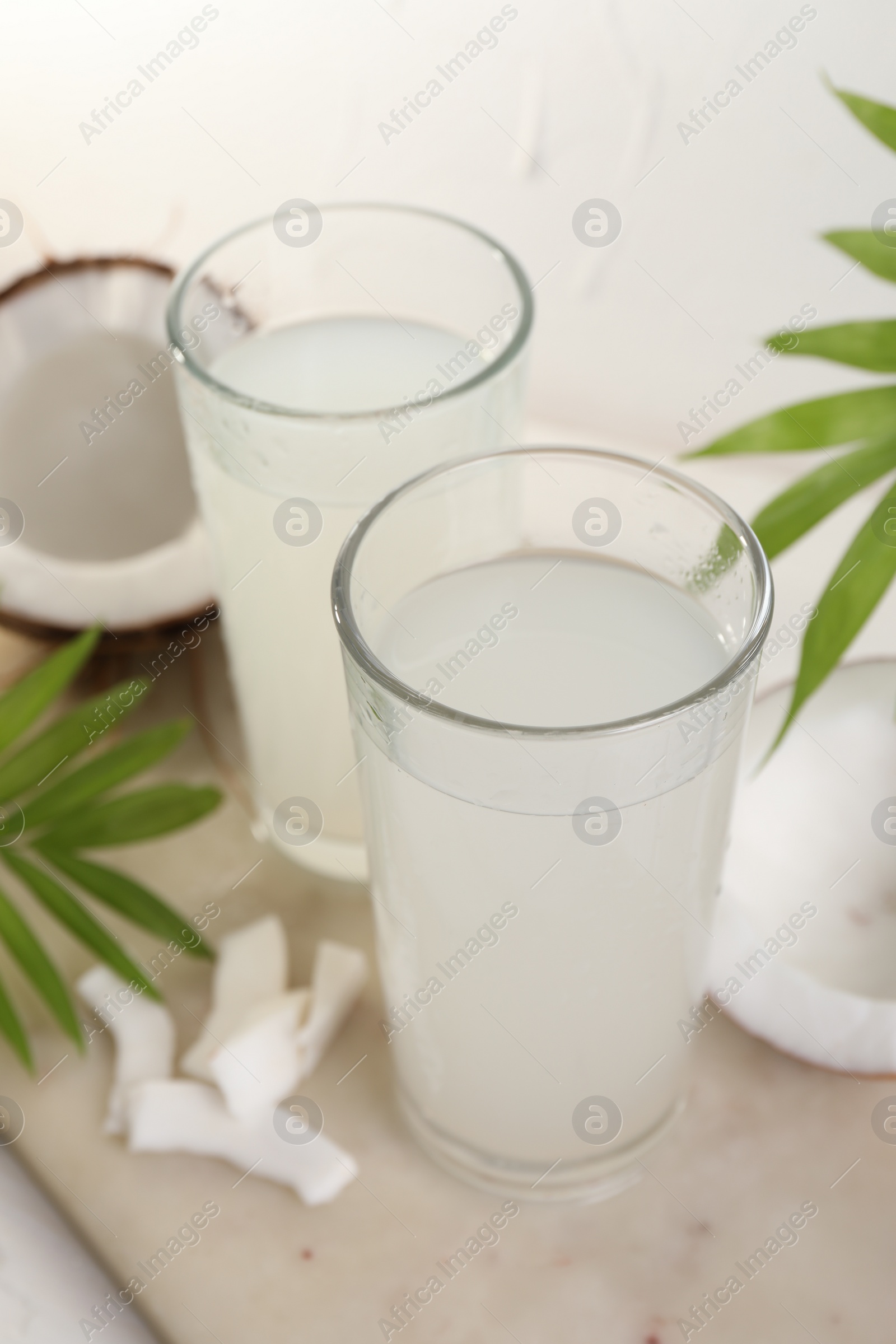 Photo of Glasses of coconut water, palm leaves and nuts on white table