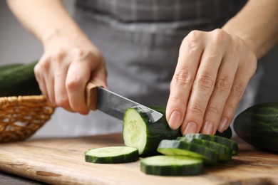 Photo of Woman cutting fresh cucumber at table, closeup