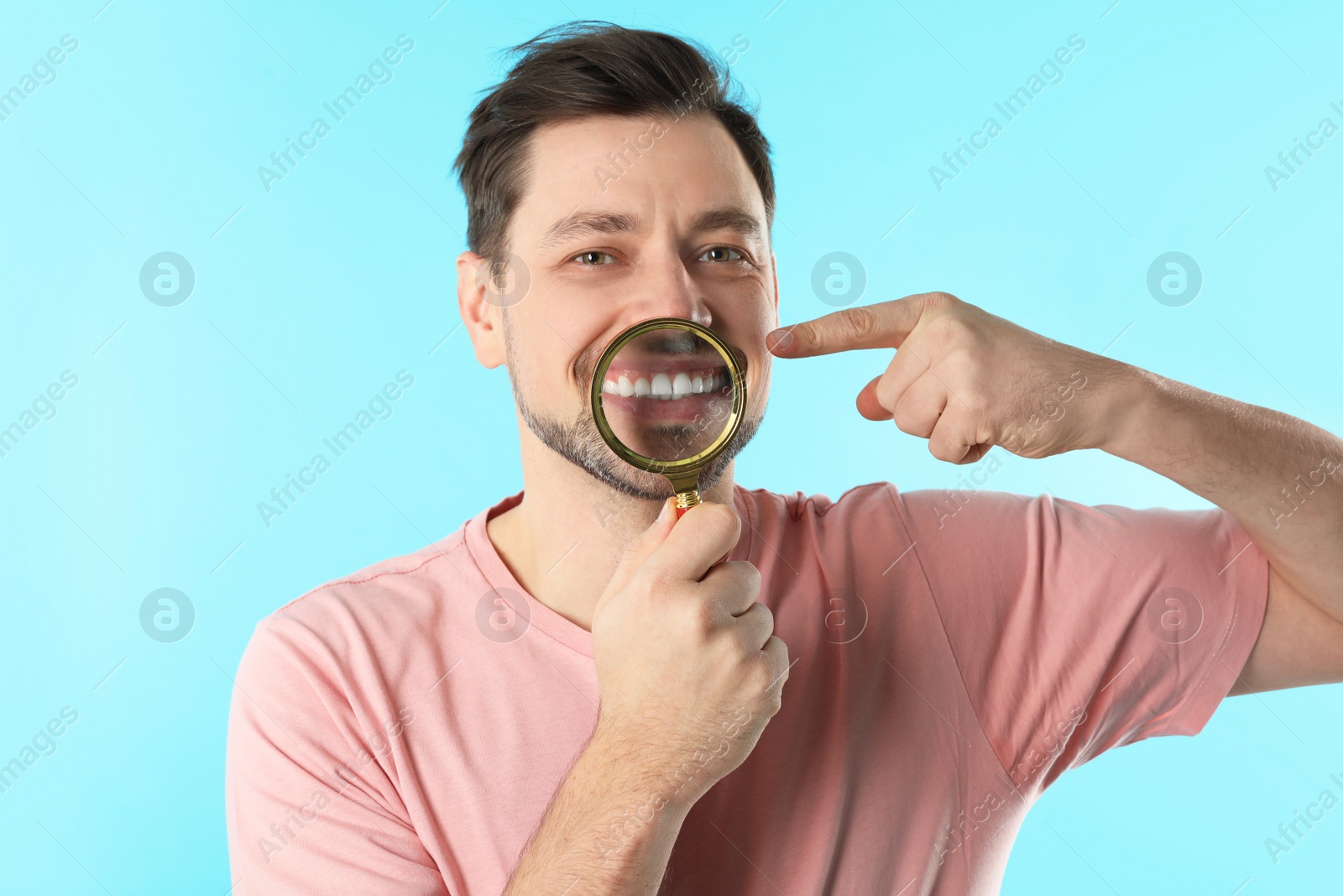 Photo of Smiling man with perfect teeth and magnifier on color background