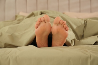 Person in bed with green linens at home, closeup on feet