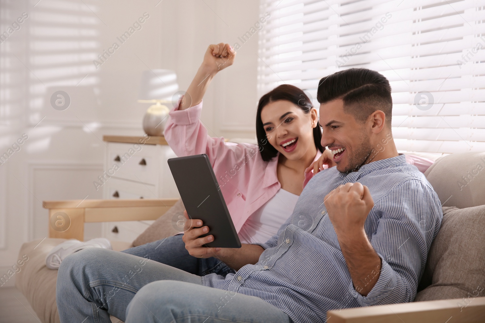 Photo of Emotional couple participating in online auction using tablet at home