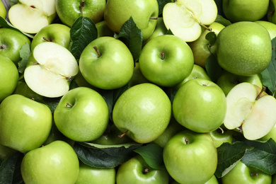 Photo of Pile of tasty green apples with leaves as background, top view