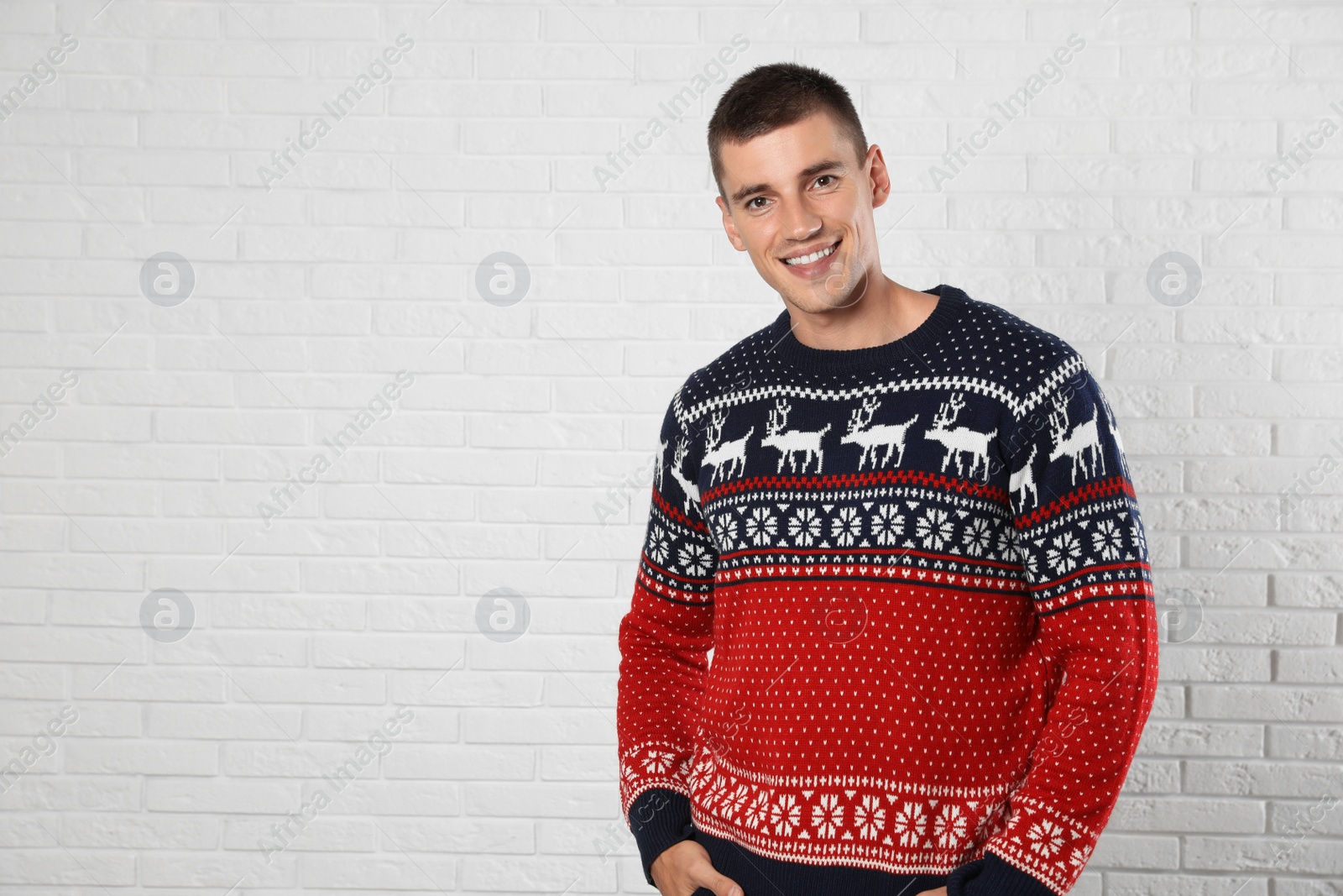 Photo of Portrait of young man in Christmas sweater near white brick wall