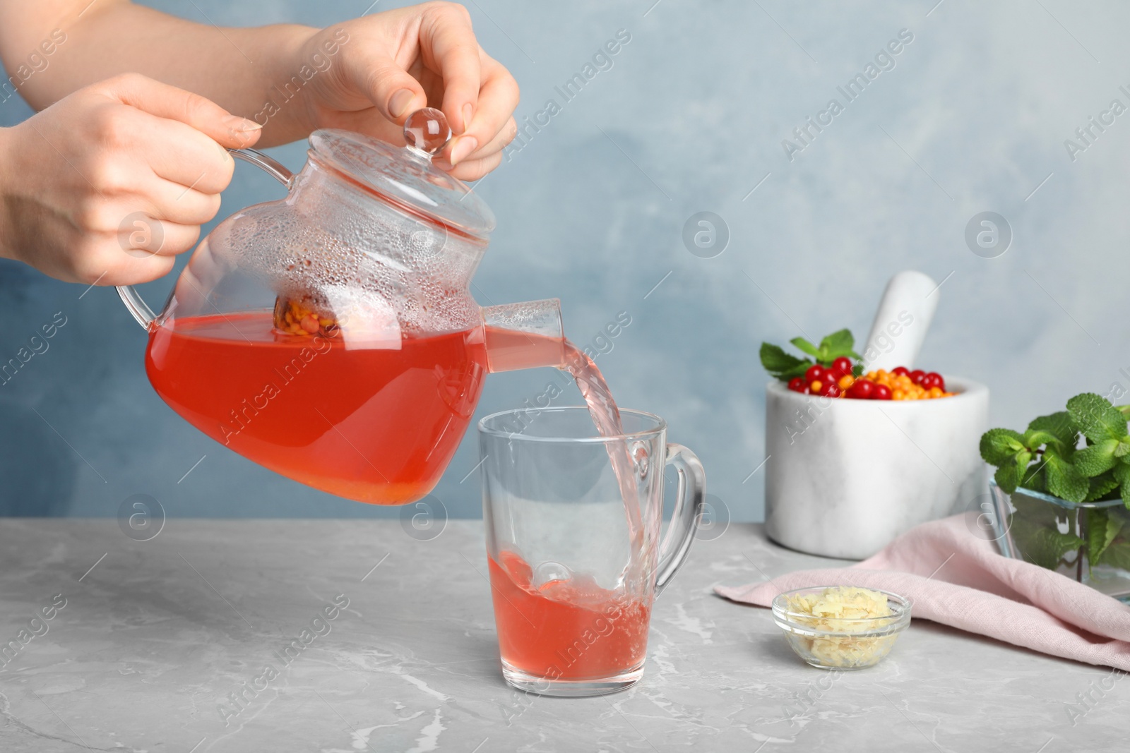 Photo of Woman pouring immunity boosting drink into cup at light grey marble table, closeup