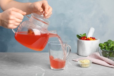 Woman pouring immunity boosting drink into cup at light grey marble table, closeup