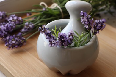 Mortar with fresh lavender flowers, rosemary and pestle on wooden table