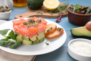 Photo of Delicious salmon tartare served with avocado and croutons on light blue table