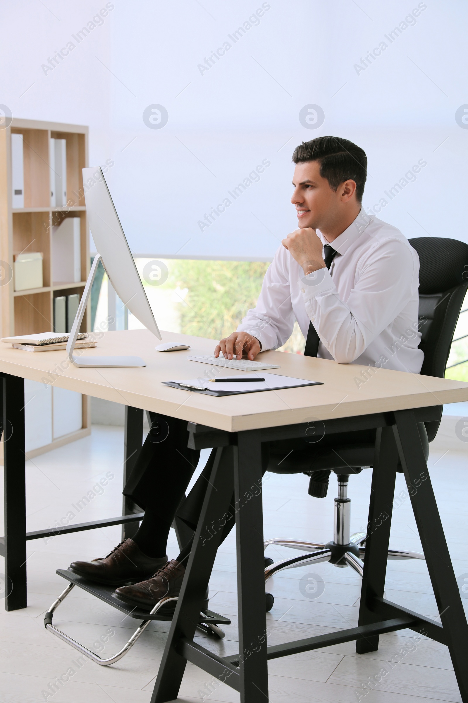 Photo of Man using footrest while working on computer in office