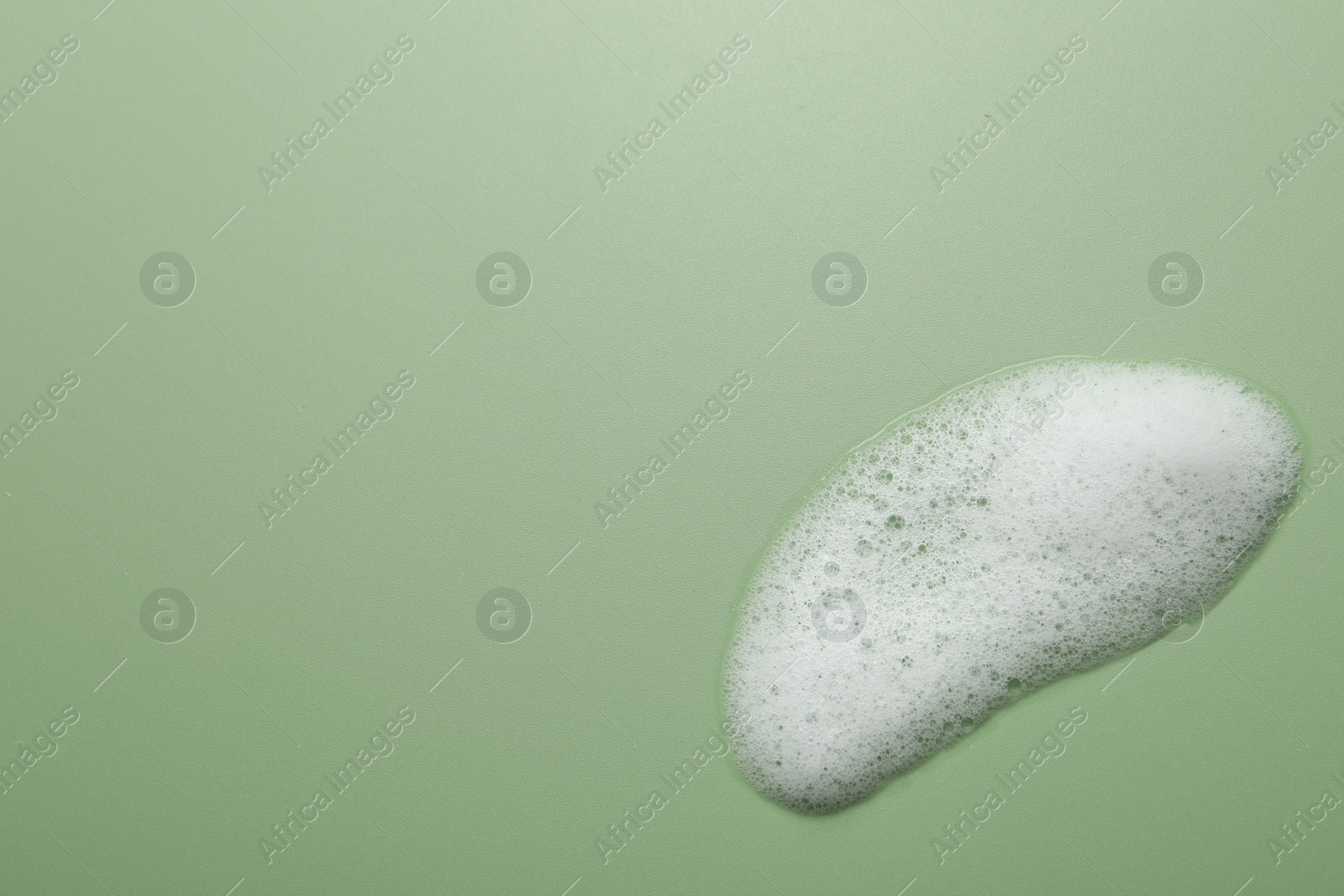 Photo of Spot of fluffy soap foam on green background, top view. Space for text