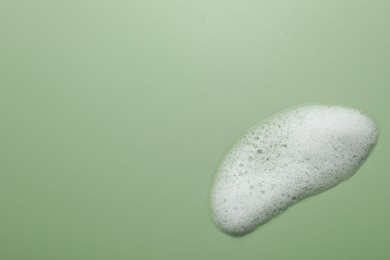 Spot of fluffy soap foam on green background, top view. Space for text