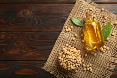 Photo of Bottle of oil and soybeans on wooden table, flat lay. Space for text