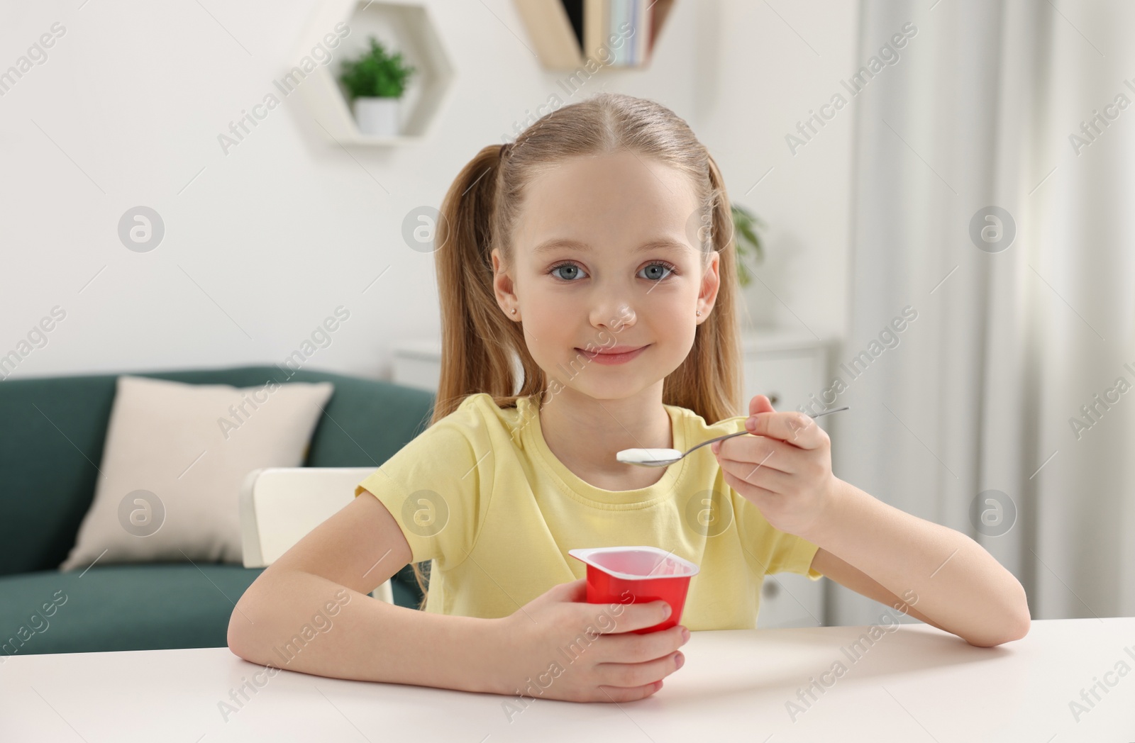 Photo of Cute little girl with tasty yogurt at white table indoors