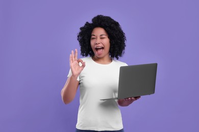 Photo of Happy young woman with laptop showing ok gesture on purple background
