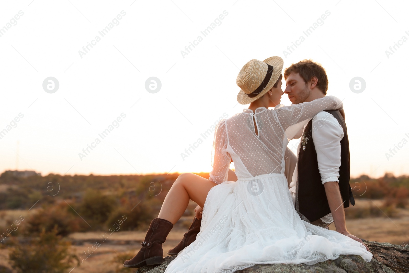 Photo of Happy newlyweds sitting on rock at sunset