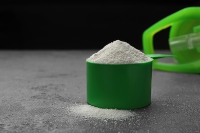 Measuring scoop of protein powder on grey stone table, closeup. Space for text