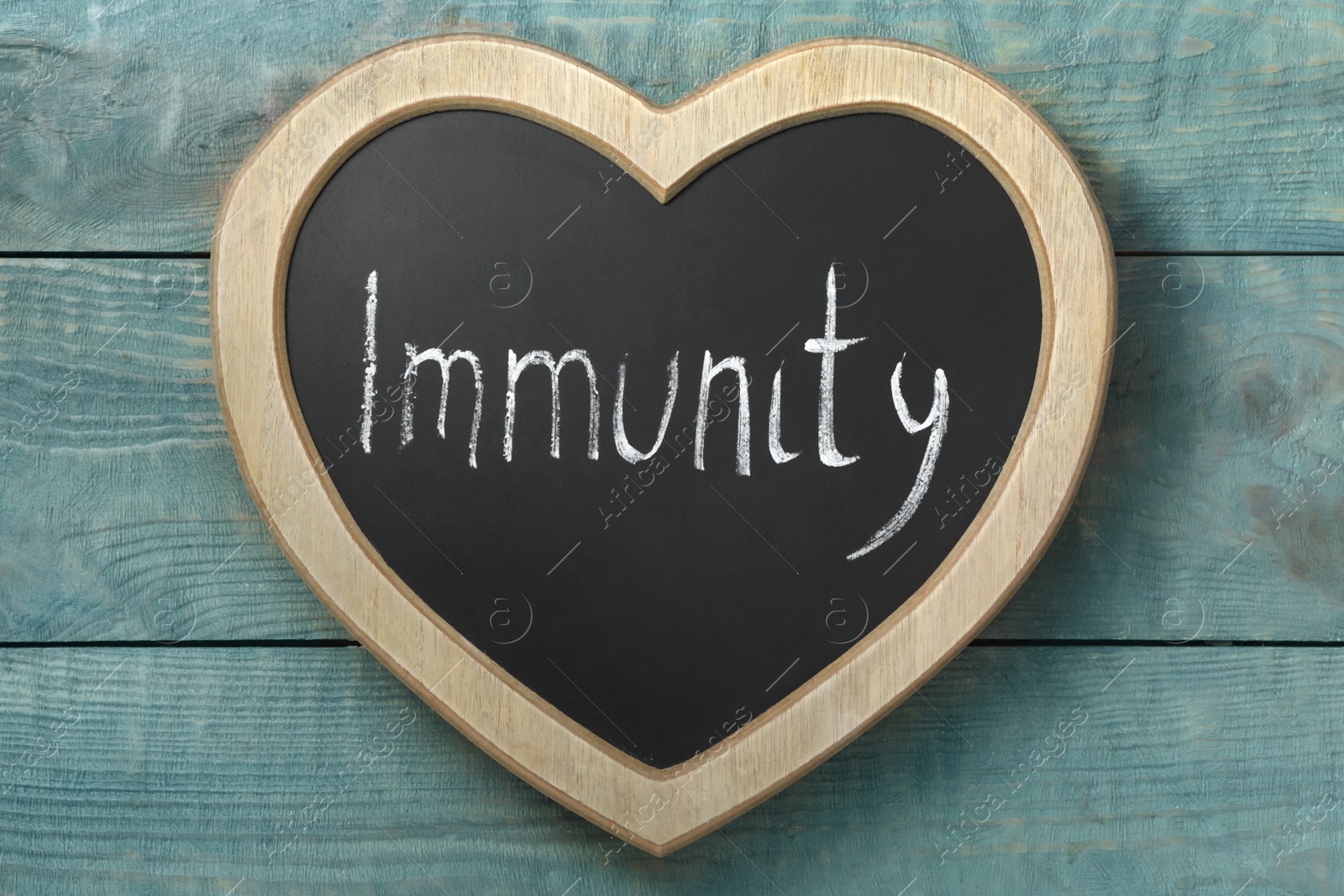 Photo of Heart shaped blackboard with word Immunity on blue wooden table, top view