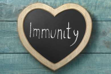 Photo of Heart shaped blackboard with word Immunity on blue wooden table, top view