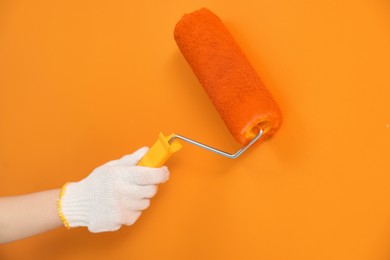 Photo of Designer painting orange wall with roller, closeup