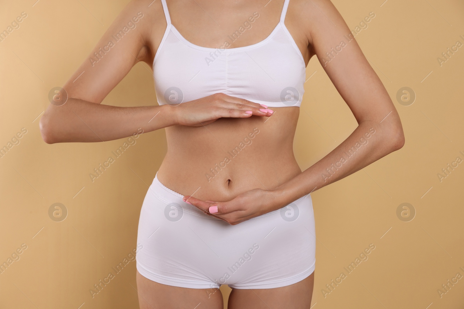 Photo of Woman in underwear holding something near her belly on beige background, closeup. Healthy stomach