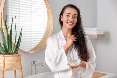 Photo of Young woman holding bowl of aloe hair mask in bathroom. Space for text