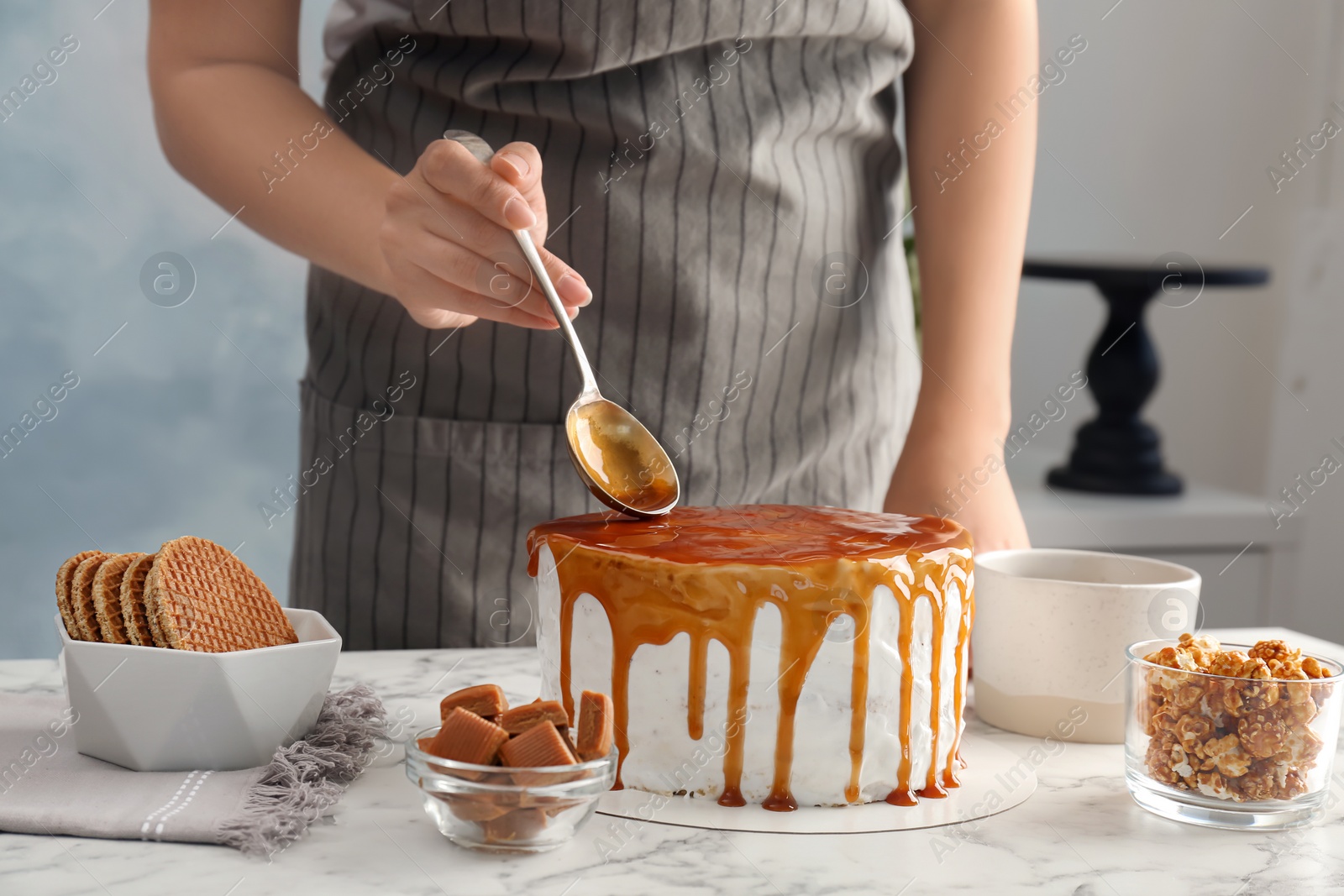 Photo of Young woman applying caramel sauce onto delicious homemade cake at table