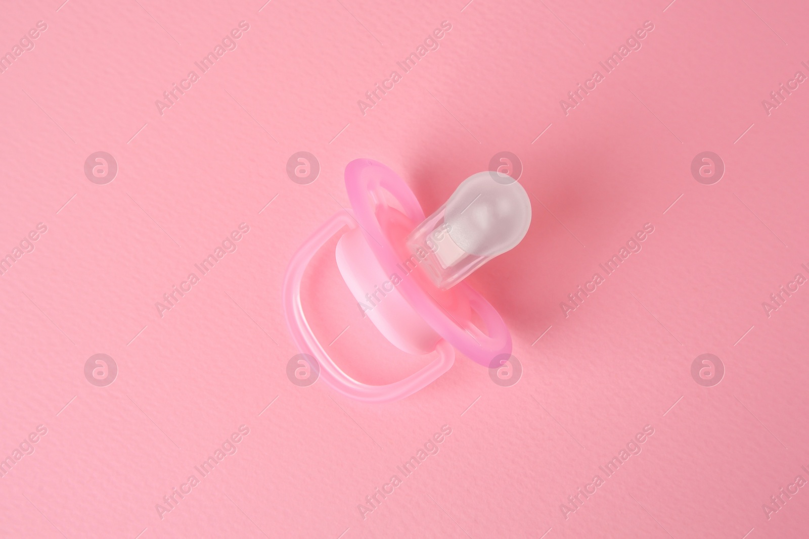 Photo of New baby pacifier on pink background, top view