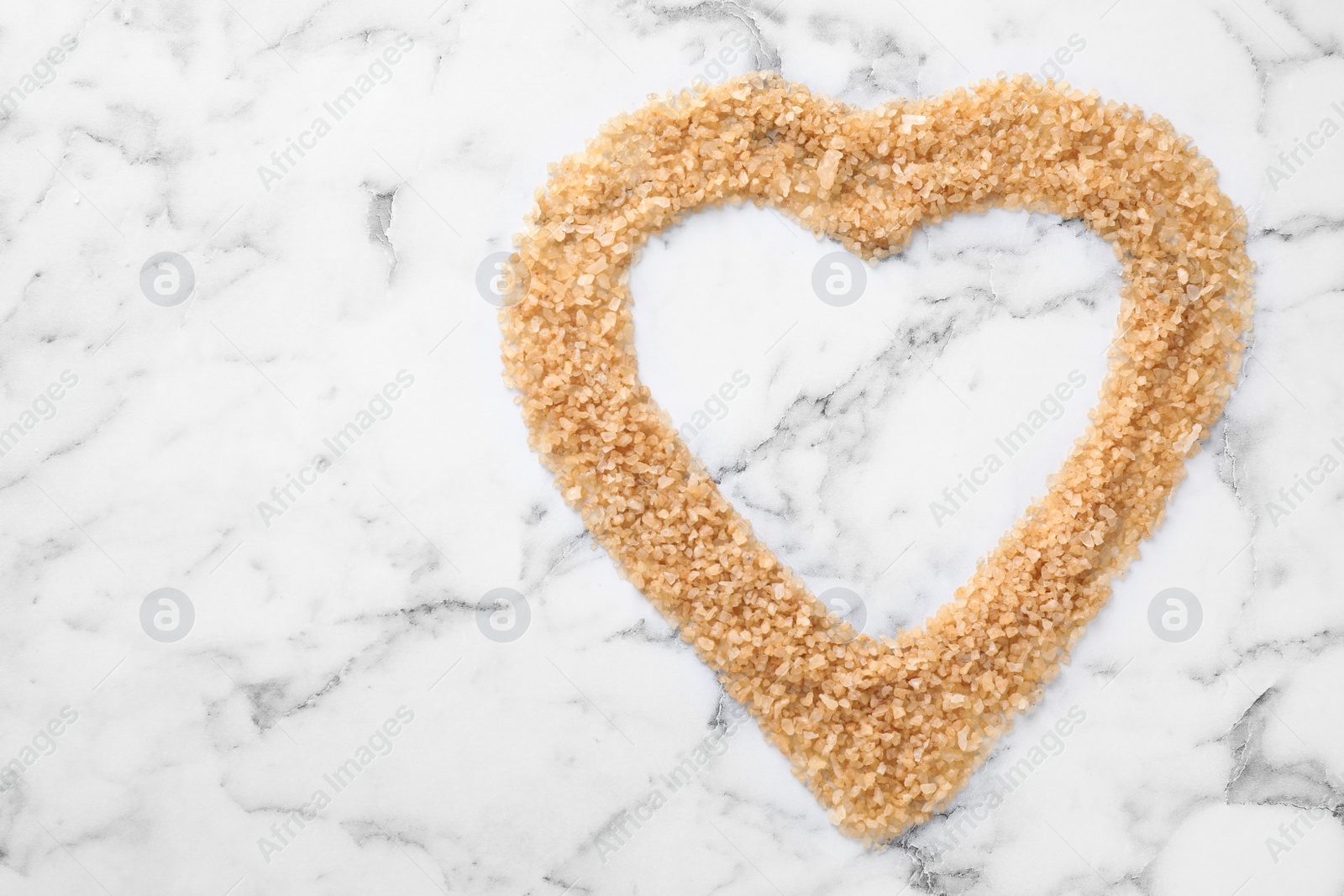 Photo of Heart made of brown sea salt on marble background, top view with space for text. Spa treatment