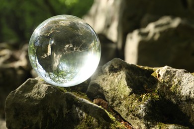 Photo of Beautiful forest with green trees, overturned reflection. Crystal ball on stone outdoors