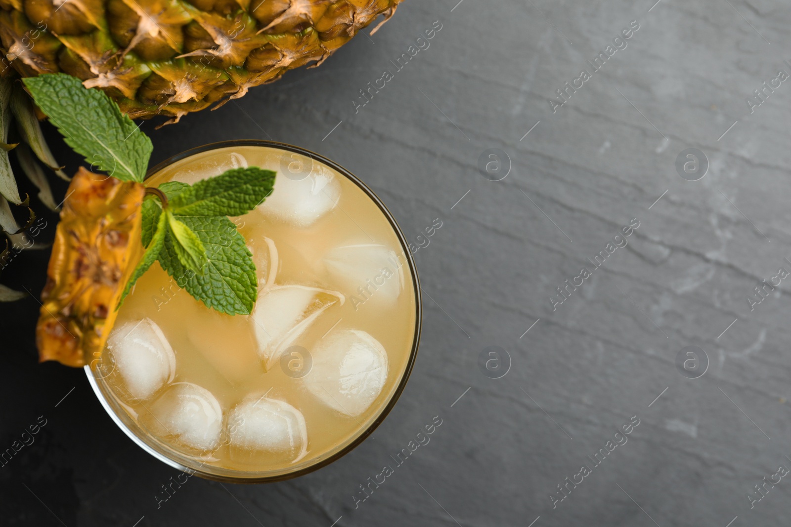 Photo of Delicious fresh pineapple juice with mint and ice cubes on black table, flat lay. Space for text