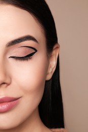 Beautiful woman with black eyeliner on beige background, closeup