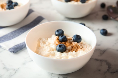 Photo of Creamy rice pudding with cinnamon and blueberries in bowl on marble table
