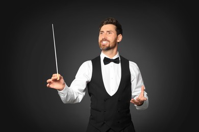 Happy professional conductor with baton on black background