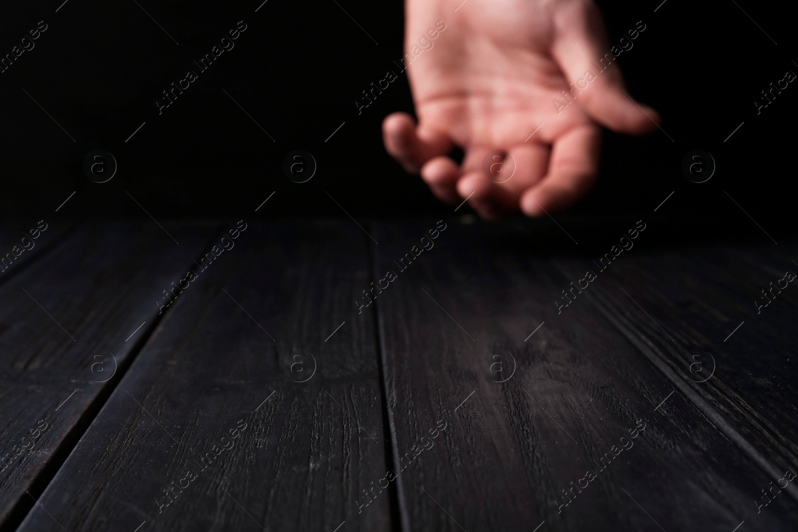 Photo of Man holding hand above black wooden table, selective focus. Space for text