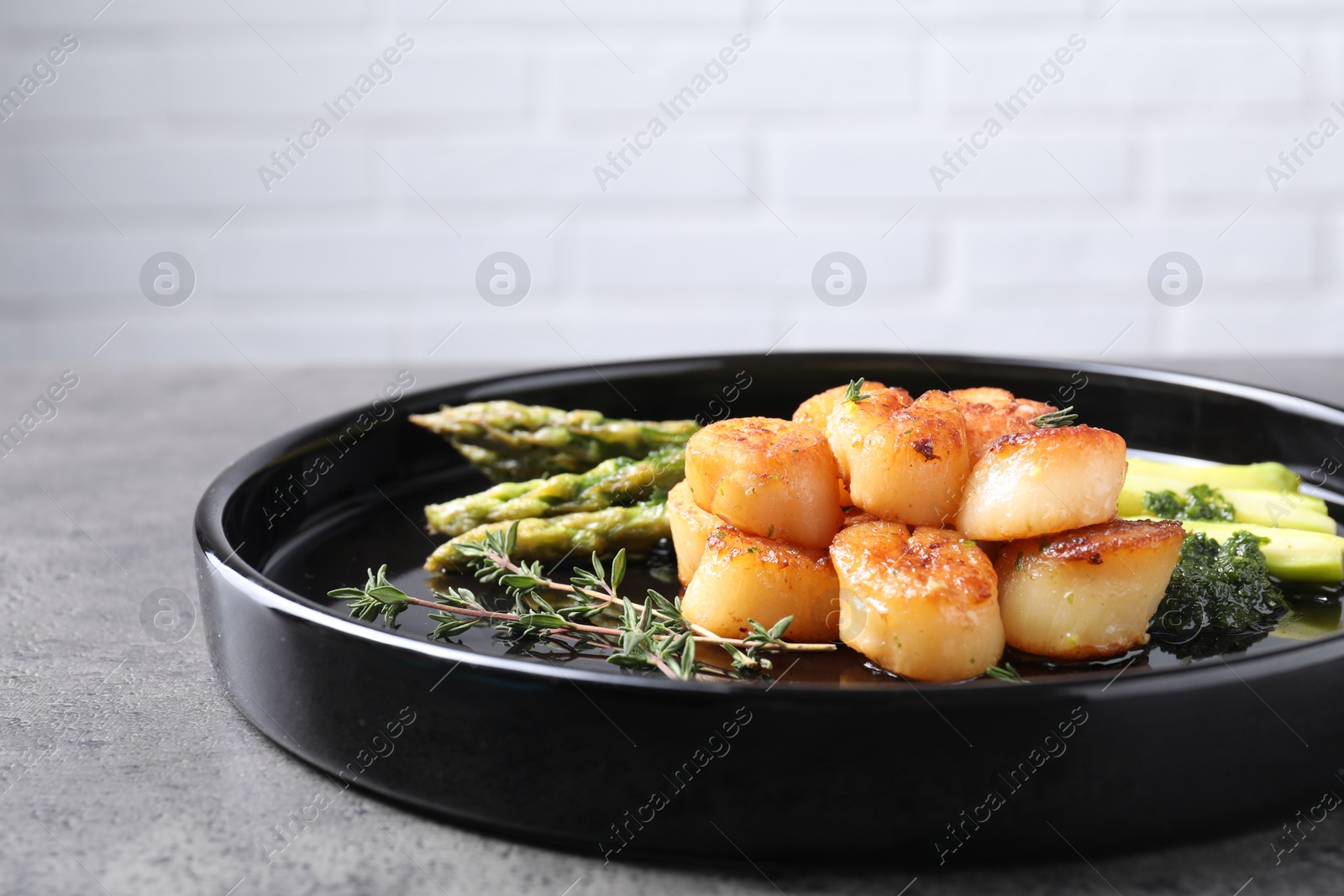 Photo of Delicious fried scallops with asparagus and thyme on grey table. Space for text