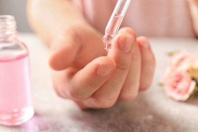 Woman dripping rose essential oil on finger at table, closeup