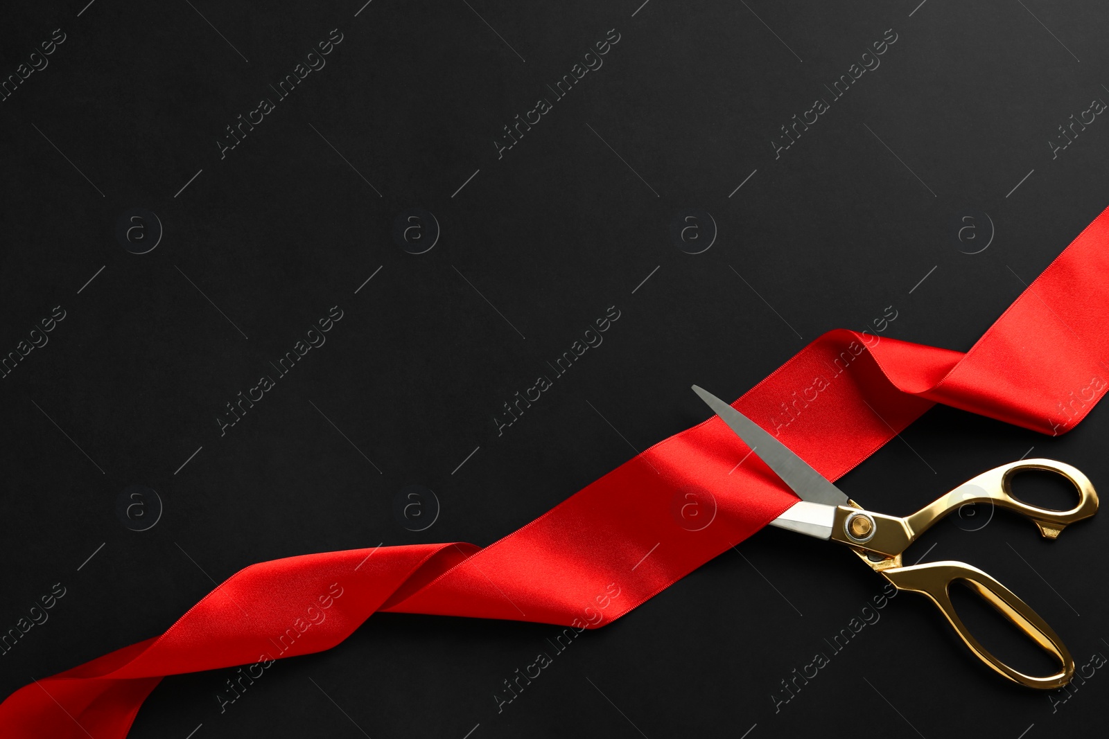 Photo of Red ribbon and scissors on black background, top view. Space for text