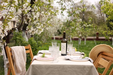 Photo of Stylish table setting with beautiful spring flowers, wine, plates and glasses in garden